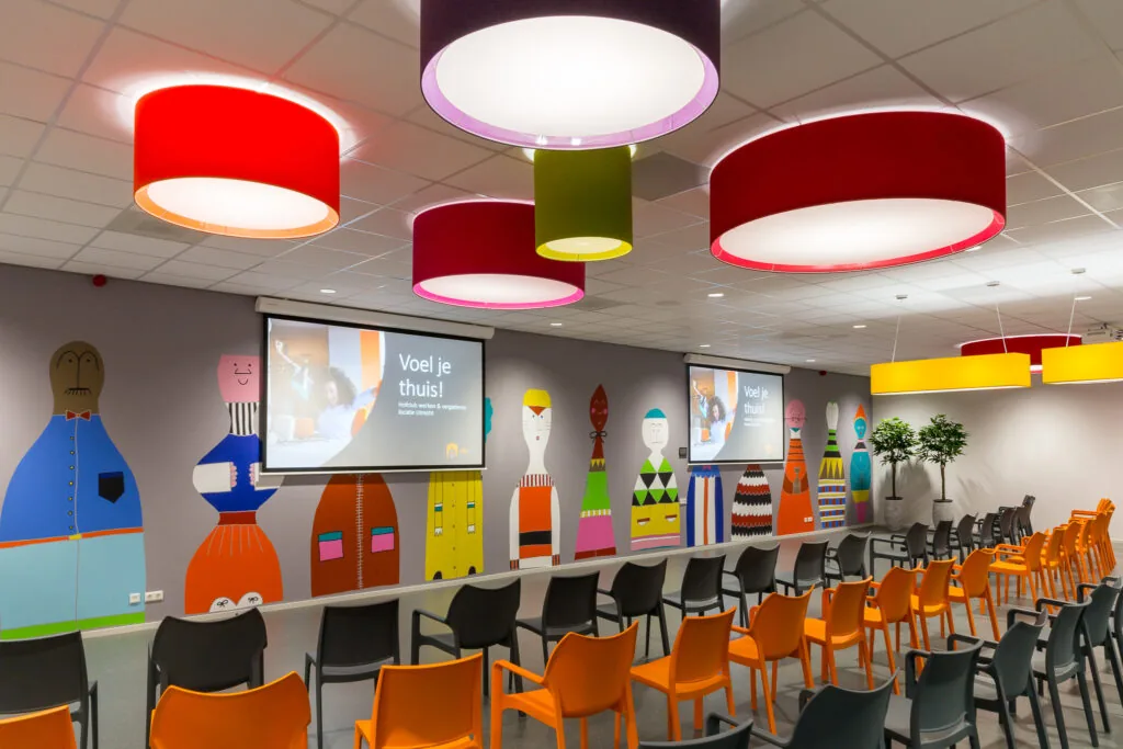 Kleurrijke presentatieruimte aan de Niels Bohrweg in Utrecht met stoelen, grote lampen en een muur vol vrolijke figuren.